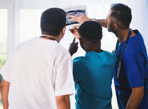 Three healthcare professionals examining an X-ray next to a window.