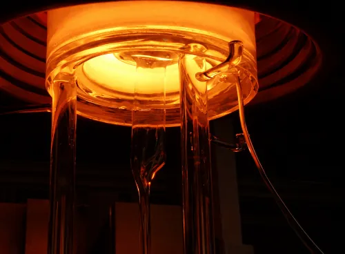 Glowing furnace with glass rods extending downward, emitting orange light.