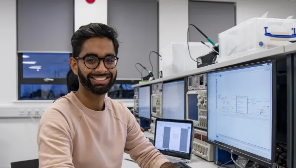 Student smiling to camera at electronics desk.