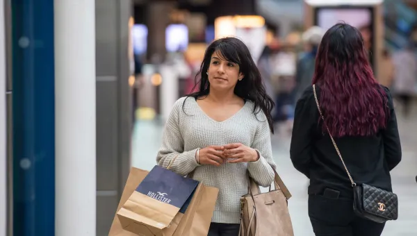 A student walking in a shopping centre whilst carrying several bags.