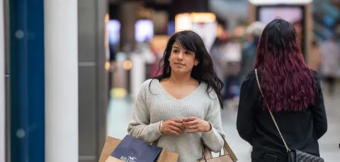 A student walking in a shopping centre whilst carrying several bags.