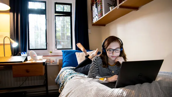 Student laying on bed, working on laptop.