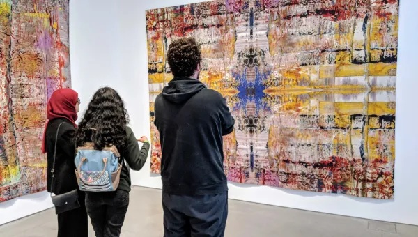 Three students admire a large piece of contemporary artwork hung on a gallery wall.