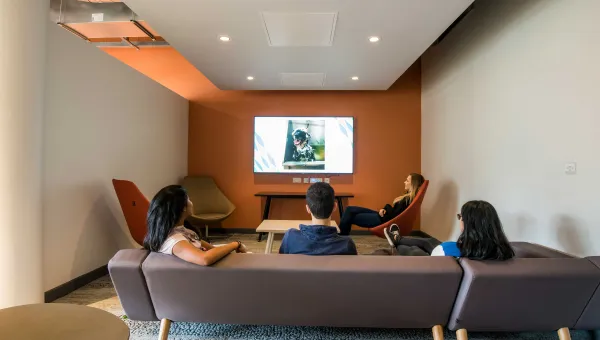 Students sitting on sofas watching large TV in shared common room.