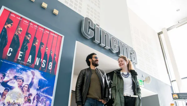 Two students walk underneath a sign reading "cinema". Movie posters adorn the walls.