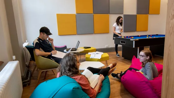 Group of students in common room, sat talking and playing pool.