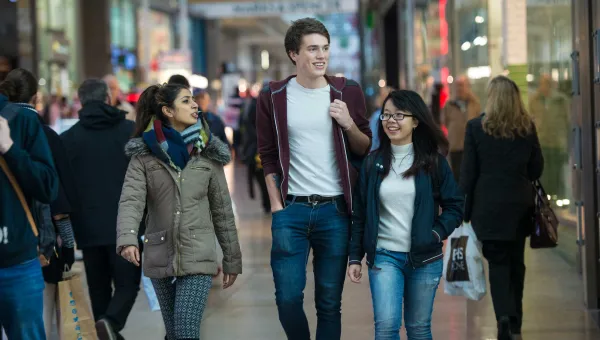Group of students walking towards camera through a crowded shopping centre.