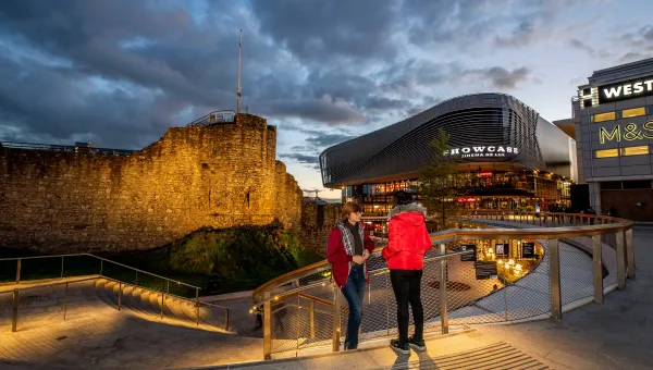 Two students stood on steps overlooking a paved plaza area with large buildings and shops.