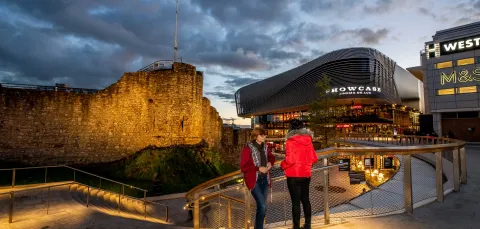 Two students stood on steps overlooking a paved plaza area with large buildings and shops.