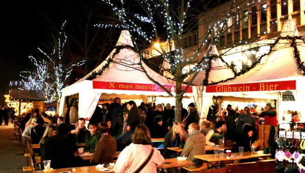 People at a refreshment stall in the Christmas market at night. 