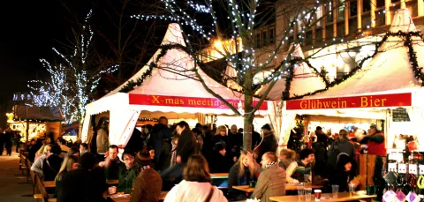 People at a refreshment stall in the Christmas market at night.