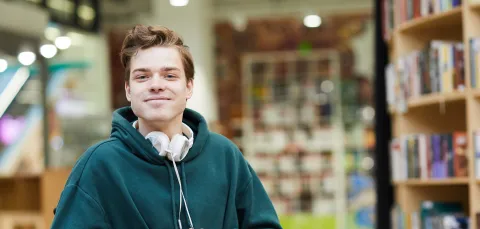 Student in wheelchair looking to camera from library. 