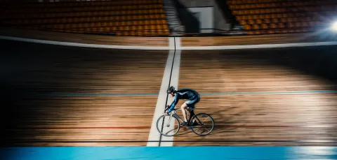 Cyclist moving fast on indoor velodrome.