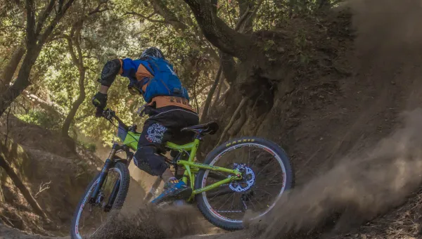 Man on mountain bike, kicking up dirt on a forest bike trail. 