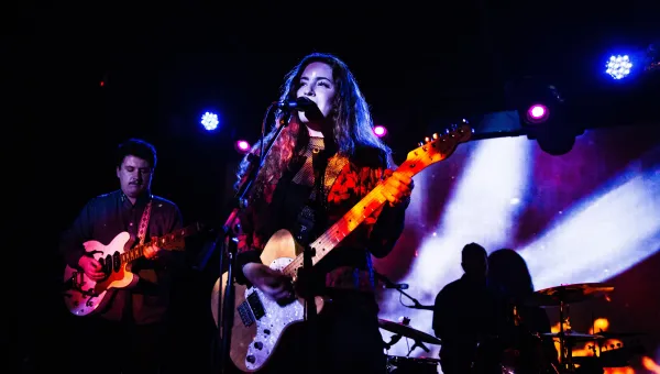 Female singer with guitar and band on small stage.