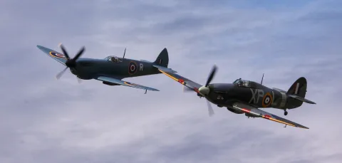 A Spitfire and a Hurricane flying in blue sky.