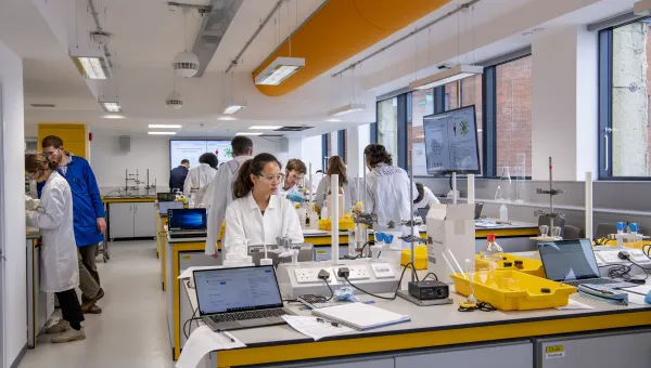 Students in lab coats working at chemistry lab benches. 