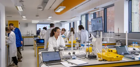 Students in lab coats working at chemistry lab benches.