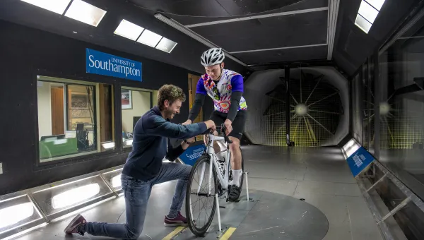 Man on bike in wind tunnel with man adjusting his wheel.