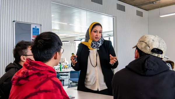 Lecturer talking to 3 students in a classroom. 