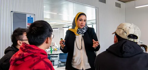 Lecturer talking to 3 students in a classroom. 