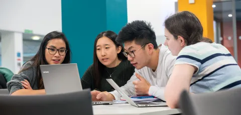 Group of animated students looking at a laptop.