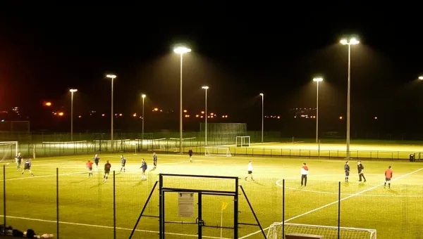 Wide view of floodlit pitches on a dark evening. A group of people are playing football.
