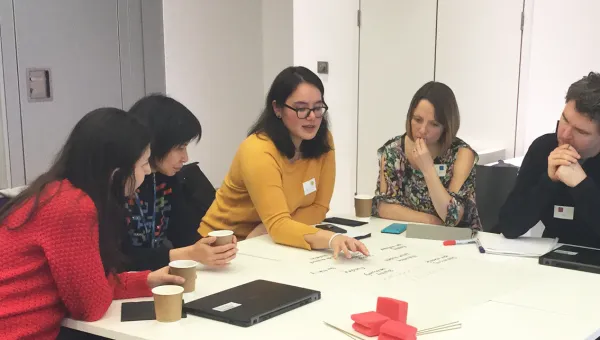 Teachers and advisers writing notes on flip chart sheets at table