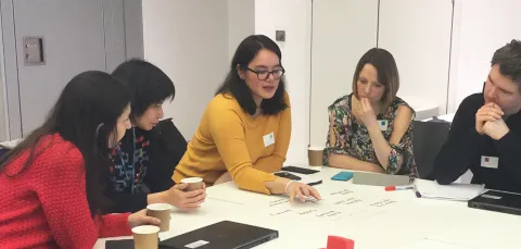 Teachers and advisers writing notes on flip chart sheets at table