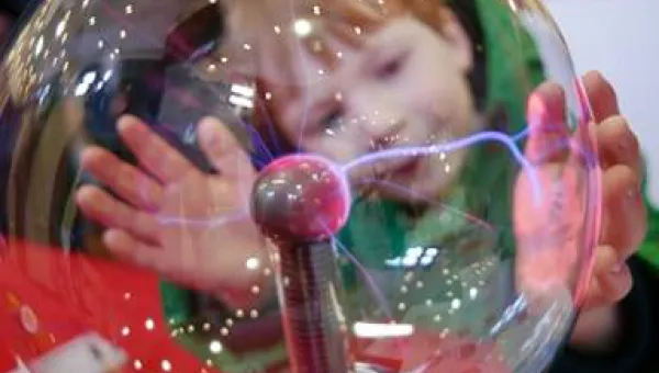 Young child with hands placed on glass electricity ball