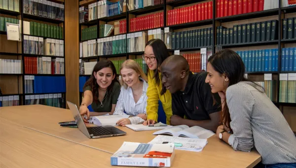Students huddle around laptop in the library law collection