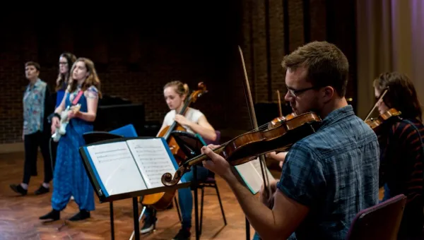 A violinist in foreground with musicians behind performing in Turner Sims