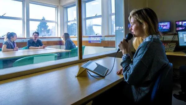 A researcher directs participants of an observation study behind a 2 way mirror