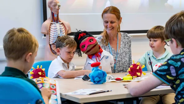 A group of primary school students doing educational activities around a table, with supervision from a member of staff.