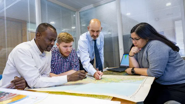 A Southampton Geospatial researcher talks with team members, standing over a map, with a laptop with a data visualisation to the side