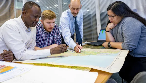 A Southampton Geospatial project team meets, with one researcher standing up, pointing to a map that his colleagues are gathered around