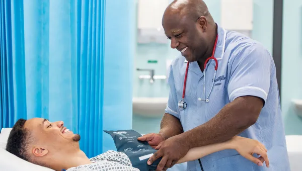 A patient and Southampton student nurse smiling at each other in a hospital room, as the nurse takes the patient's blood pressure.