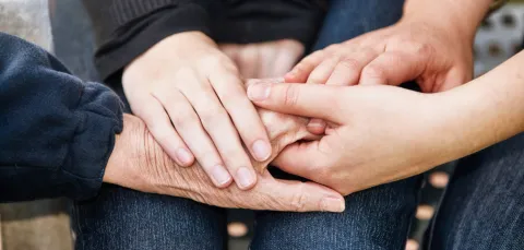 A close up of several overlapping hands holding each other, representing young, mid-life and older generations.