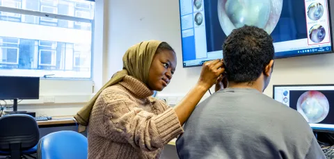 Audiology student looking into a persons ear and showing it on a big screen