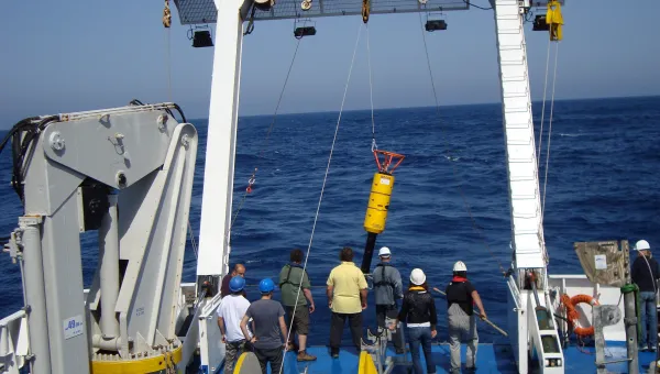 A team onboard a ship lifts an instrument into the water to measure ocean turbulence