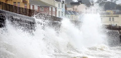 Waves crashing on a sea wall opposite houses