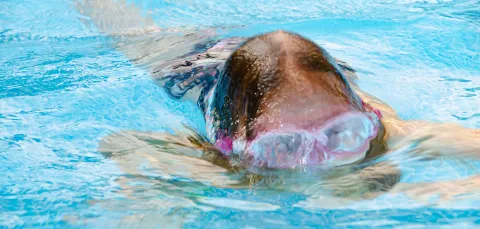 Close up of a child in a swimming pool, their goggles features peeping above the water