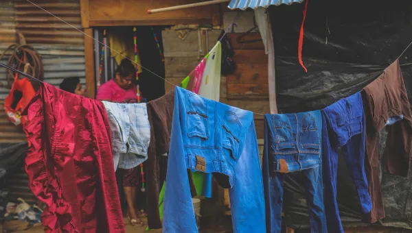 Woman walking past numerous people sitting along a fence covered in laundry