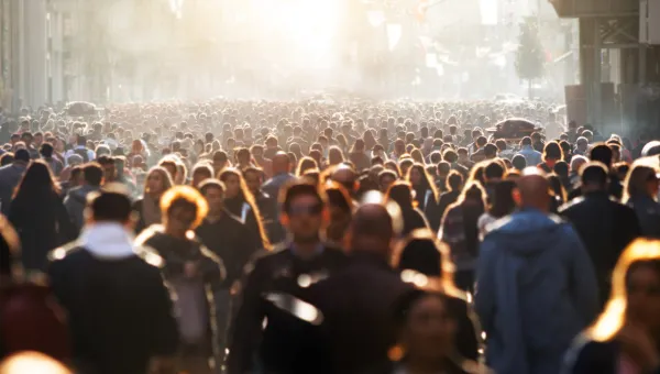 A large crowd of people spans from the foreground to the background. The people closer to us are picked out as indviduals because of a low, bright sunlight.