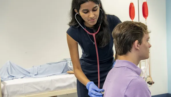 An undergraduate medicine student practices using a stethoscope on a patient in the clinical skills suite