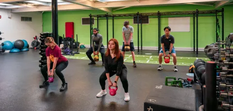 People in a gym lifting a kettlebell from a squatting position