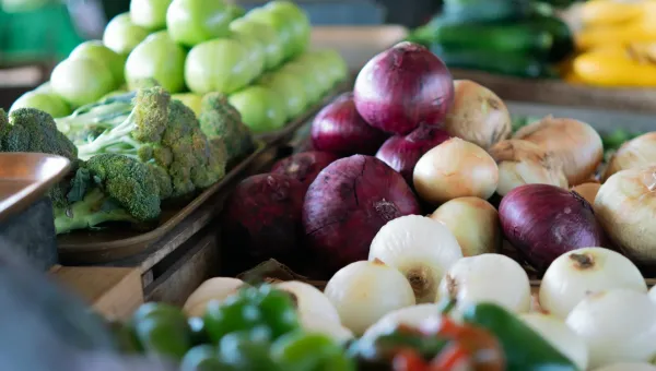 Assorted vegetables including onions, bell peppers, broccoli, and beetroot on a market stand.