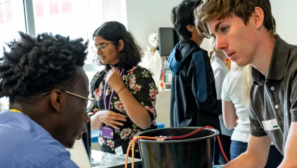 Four people in a medical training session, with one practicing a procedure on a manikin arm while others converse in the background, indicating a focus on skill development and collaboration.