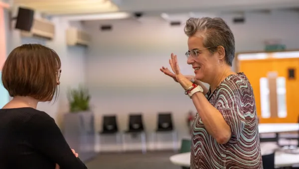 Two people are having an animated discussion. The one on the right is holding both hands up and is smiling. The one on the left has her arms folded and seems to be listening. 