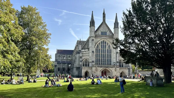 Exterior of Winchester cathedral with several people sat in the surrounding grounds.